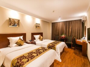 A hotel room with two beds, a desk, a chair, and a small table with a plant.