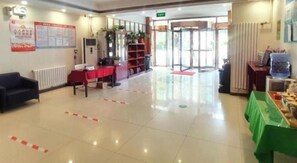A hotel lobby with a reception desk, seating area, and a glass door entrance.