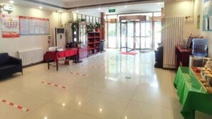 A hotel lobby with a reception desk, a red table, a sofa, a bookshelf, and a green table with items on it. - Greentree Inn Beijing Daxing District Yufa Town Ne (Daxing)