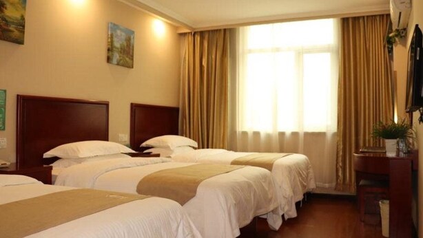 A hotel room with two beds, a wooden headboard, a large window with curtains, and a small desk with a plant. - Greentree Inn Beijing Daxing District Yufa Town Ne (Daxing)
