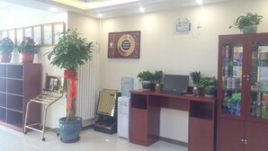 A reception area with a desk, computer, potted plants, a radiator, and a cabinet with glass doors. - Greentree Inn Beijing Daxing District Yufa Town Ne (Daxing)