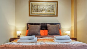 Una habitación de hotel con una cama grande, dos almohadas, un cabecero, lámparas de noche y un cuadro en la pared.