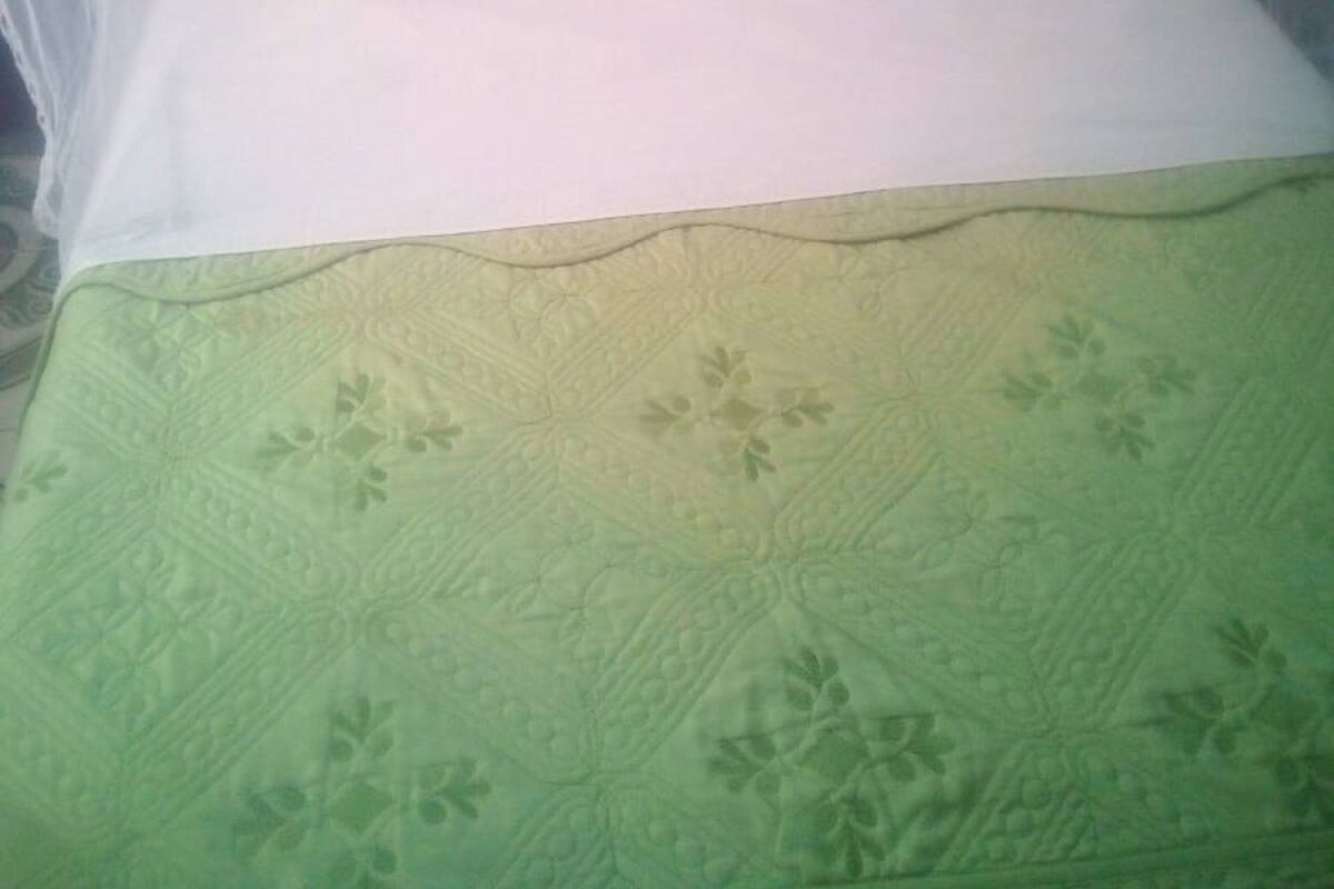 A bed with a white mattress and a green quilt.