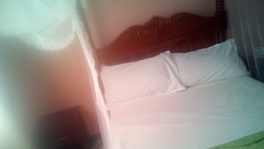 A bed with white bedding and a green patterned cover, a wooden headboard, and a wall with a decorative plate. - Famouse Guest House (Nairobi)