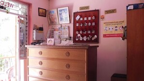 A hotel room with a wooden dresser, a desk with a computer, a window with a view, and a door with a sign. - Hotel Bharat Palace (Jaipur)