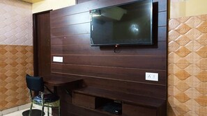 Una habitación con un panel de madera oscura en la pared, un televisor de pantalla plana sobre una mesita pequeña y un enchufe en la pared.