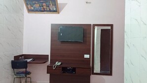 A room with a wooden TV stand, a small table with a chair, and a mirror. - Hotel Bharat Palace (Jaipur)