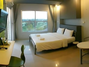 A hotel room with a bed, a desk, a chair, a round table, and a large window with a view. - A Hotel (Ubon Ratchathani)