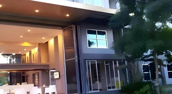 Un edificio moderno con un gran ventanal, un balcón y un árbol en primer plano.