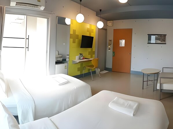 Habitación de hotel con dos camas, un escritorio, una silla, una mesita y un televisor en la pared.