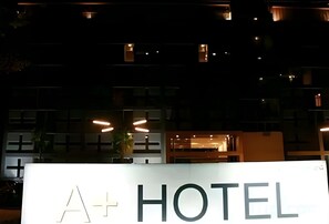 Señalización de 'A+ HOTEL' con un edificio moderno al fondo.