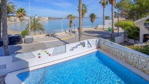 A swimming pool with a view of the sea, palm trees, and a road with a car parked nearby. - Rocamar by Interhome (Calpe/Calp)