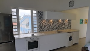 Une cuisine moderne équipée d’un four encastré, d’un lave-linge et d’une fenêtre donnant sur des immeubles.