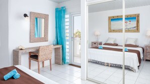 Une chambre d’hôtel avec un lit, un bureau, une chaise, un miroir, un tableau et une vue sur l’extérieur, visible à travers une porte vitrée.