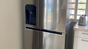 Un réfrigérateur en acier inoxydable doté d’un distributeur d’eau, un grille-pain et une fenêtre avec des rideaux.