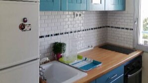 Une cuisine avec des meubles de couleur turquoise, un réfrigérateur blanc, un plan de travail en bois et un lave-vaisselle noir.