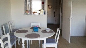 Un coin repas avec une table ronde et des chaises blanches, un bol bleu et une chaise blanche avec un coussin bleu.