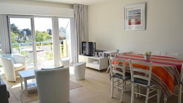 Une chambre d’hôtel avec un balcon, un coin repas avec une table et des chaises, une télévision et un tableau au mur.