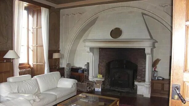 Een woonkamer met een witte bank, een glazen salontafel en een open haard.