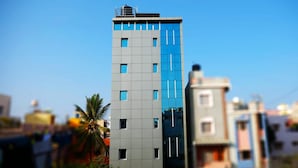 A modern multi-story building with a mix of glass and concrete facade, featuring a prominent water tank on the roof. - The Ventura Grand Hotel (Bengaluru)