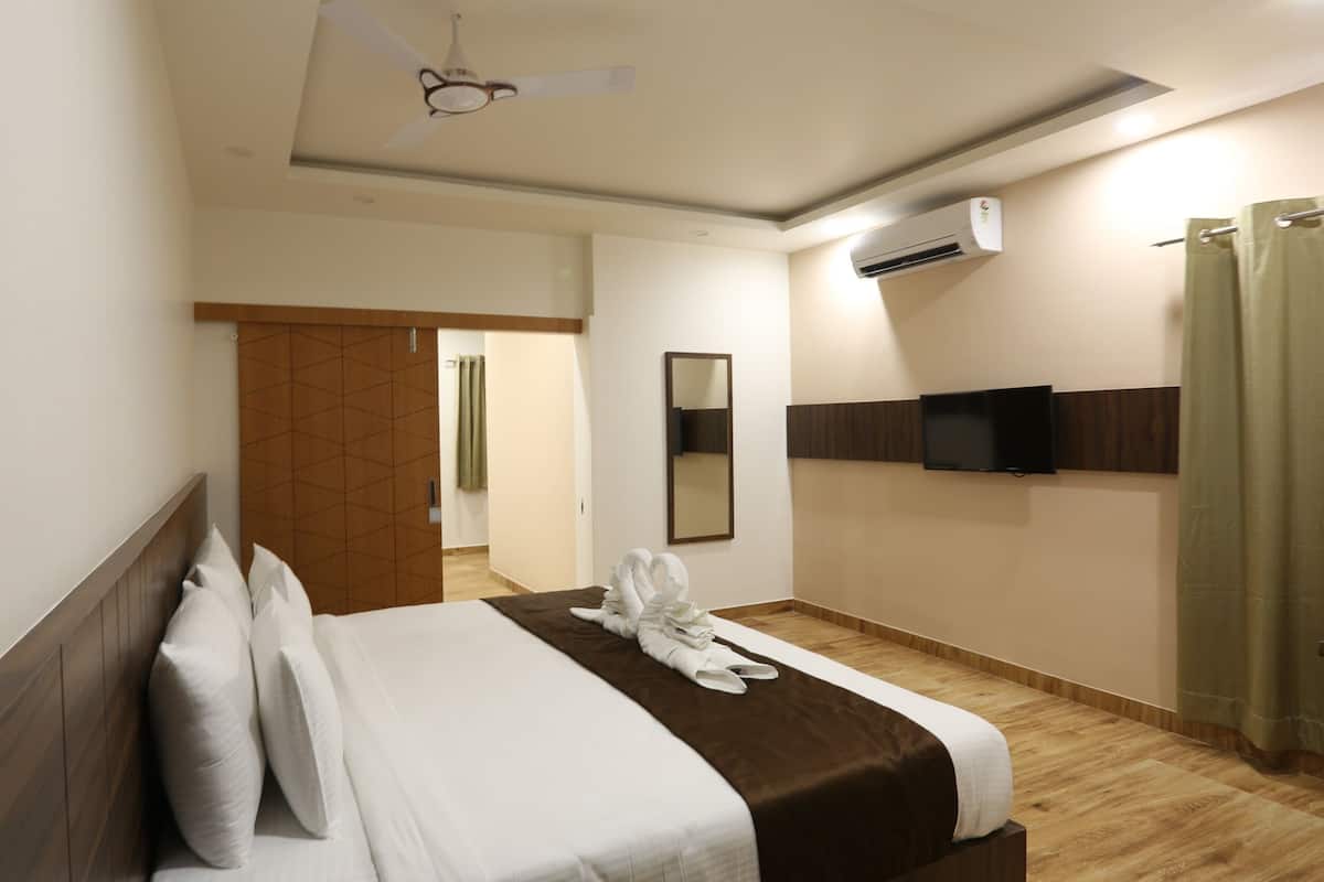 Habitación de hotel con cama, ventilador de techo, unidad de aire acondicionado, televisión y baño con cortina de ducha.