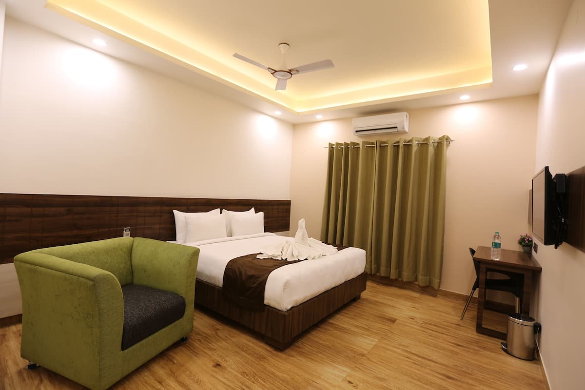 Una habitación de hotel con cama, un sillón verde, un escritorio con silla, un equipo de aire acondicionado y un ventilador de techo.