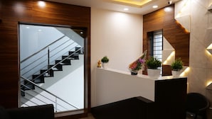 A modern interior with a glass staircase, a reception desk with plants, and a wooden accent wall. - The Ventura Grand Hotel (Bengaluru)