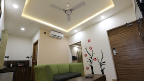 A modern living room with a green sofa, a wooden coffee table, and a ceiling fan. - The Ventura Grand Hotel (Bengaluru)