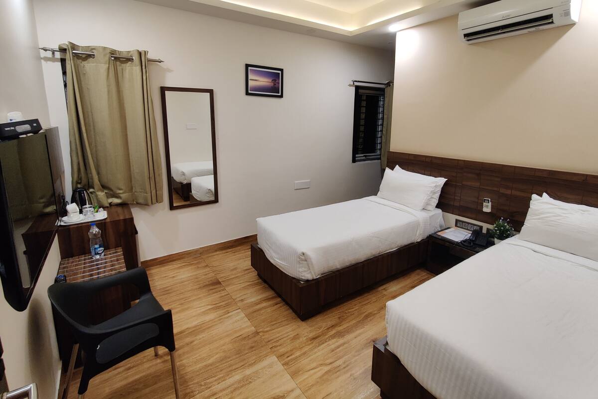Habitación de hotel con dos camas, un escritorio con silla, un espejo, aire acondicionado y ventilador de techo.