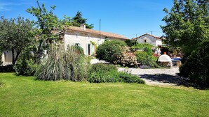 A stone house with a tiled roof, surrounded by a well-maintained garden with various shrubs and a lawn. - Luxurious private gite with pool, terrace, large gardens, golf simulator and gym (Limalonges)