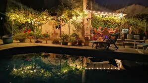 A nighttime outdoor patio area with a pool, stone walls, and string lights. - Luxurious private gite with pool, terrace, large gardens, golf simulator and gym (Limalonges)