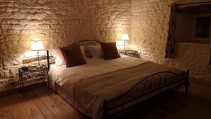 A bedroom with a stone wall, a wooden floor, a metal bed frame, and two bedside tables with lamps. - Luxurious private gite with pool, terrace, large gardens, golf simulator and gym (Limalonges)