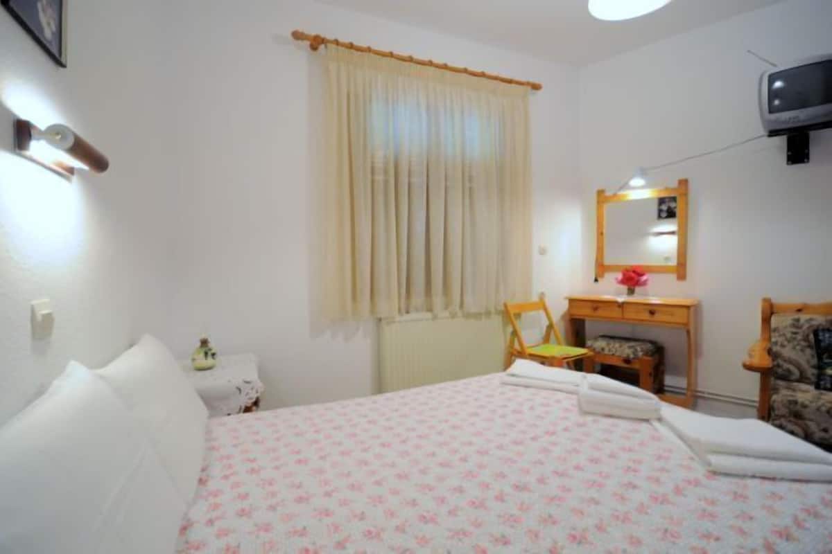 Een slaapkamer met een bed, een stoel, een klein tafeltje, een spiegel en een televisie.