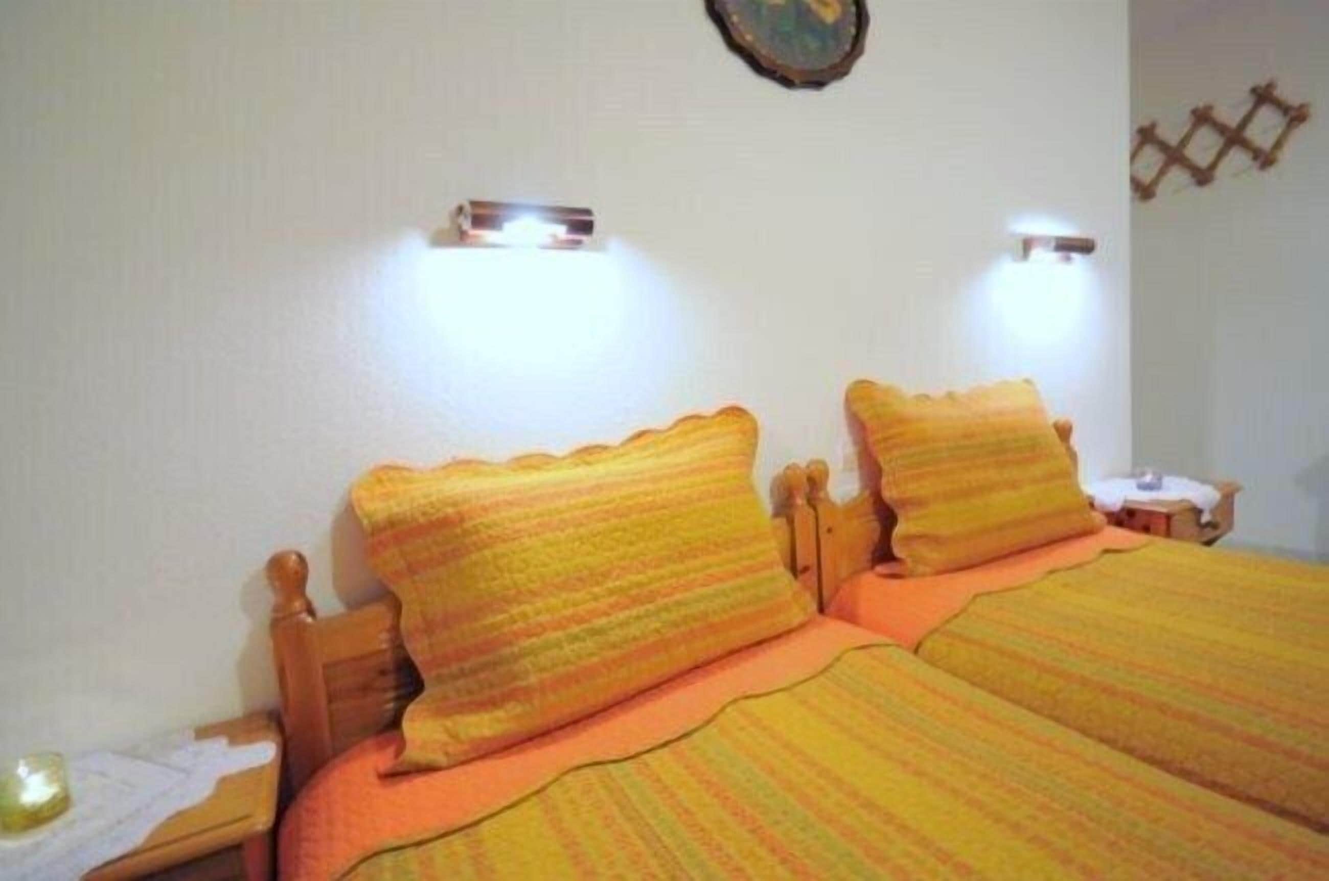 Une chambre avec deux lits, chacun doté d’une tête de lit en bois et d’une literie orange. On y trouve deux tables de chevet avec des lampes.