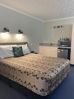 Un dormitorio con cama, mesita de noche, escritorio con microondas y una pequeña kitchenette.