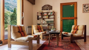 A cozy living room with two armchairs, a coffee table, and a bookshelf filled with books. A large window offers a view of a mountainous landscape. - Le Belvédère (Brides-les-Bains)