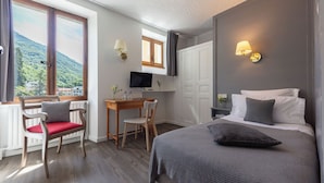 A hotel room with a bed, a desk, a chair, a TV, and a window with a view of a mountain. - Le Belvédère (Brides-les-Bains)