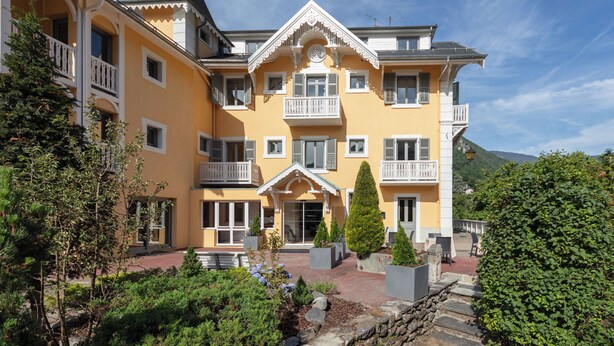 A multi-story building with balconies, a central entrance, and surrounding greenery. - Le Belvédère (Brides-les-Bains)