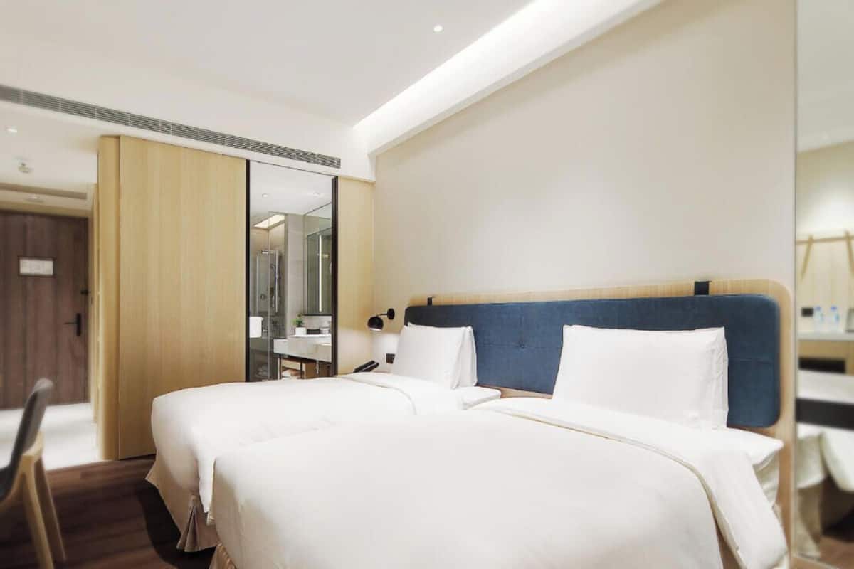 A hotel room with a large bed, a desk, a chair, and a mirror.