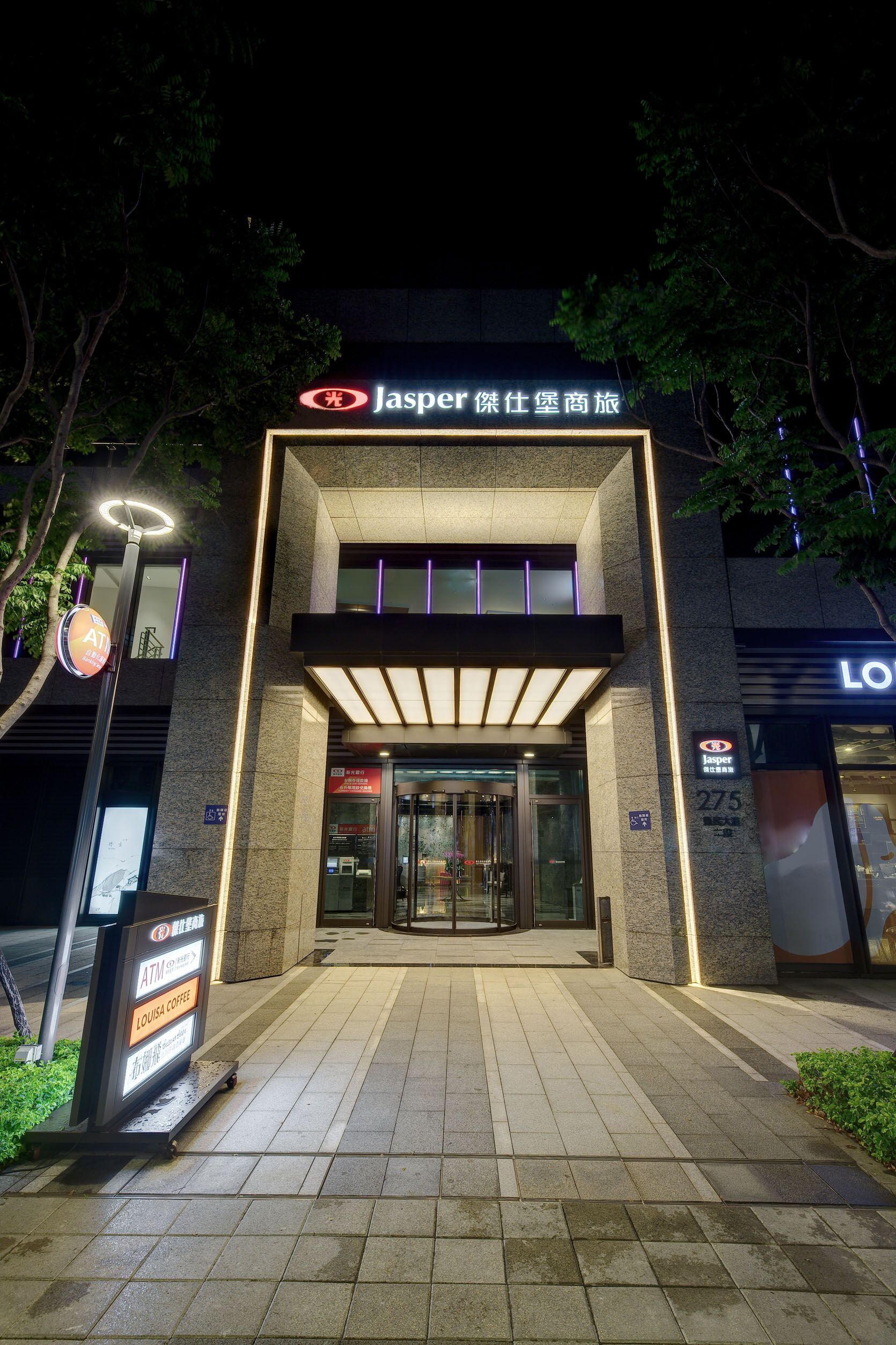 A Jasper hotel entrance with a modern design, including a glass door and a signboard with amenities like ATM and coffee.
