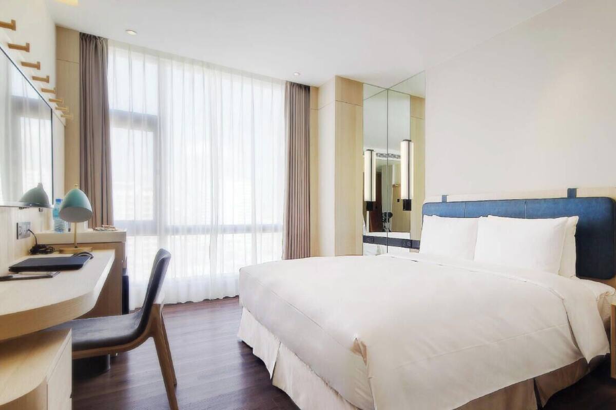 A hotel room with a bed, desk, chair, and a mirror.