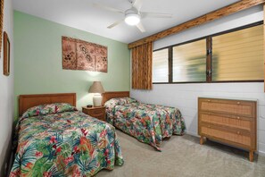 Une chambre avec deux lits, un ventilateur de plafond, une fenêtre avec des stores, une commode en bois et une œuvre d’art accrochée au mur.