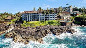A coastal hotel with multiple buildings, a rocky shoreline, and clear blue waters. - Captivating Ocean Front Condo Living-Poipu Shores (POIPU)