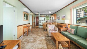 Un amplio salón con sofá, mesas de madera y una cocina al fondo.