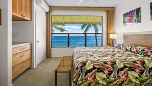 Un dormitorio con cama, ventana con vista al océano, ventilador de techo y armario de madera.