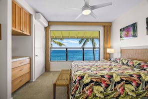 Une chambre à coucher avec un lit, une fenêtre donnant sur l’océan, un ventilateur de plafond et une armoire en bois.