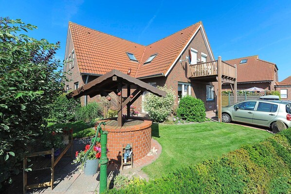 A residential house with a brick facade, a sloped roof, and a small garden area with a wooden structure.