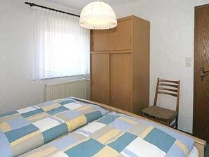 A bedroom with a bed, a wooden wardrobe, a chair, and a window with curtains.