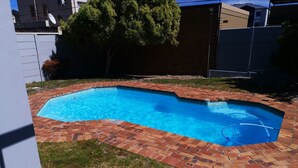 A rectangular swimming pool with a brick border, surrounded by grass and a brick patio. - The Sands B32 (Cape Town)