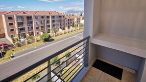 A balcony with a view of a multi-story apartment building, a road, and some greenery. - The Sands B32 (Cape Town)